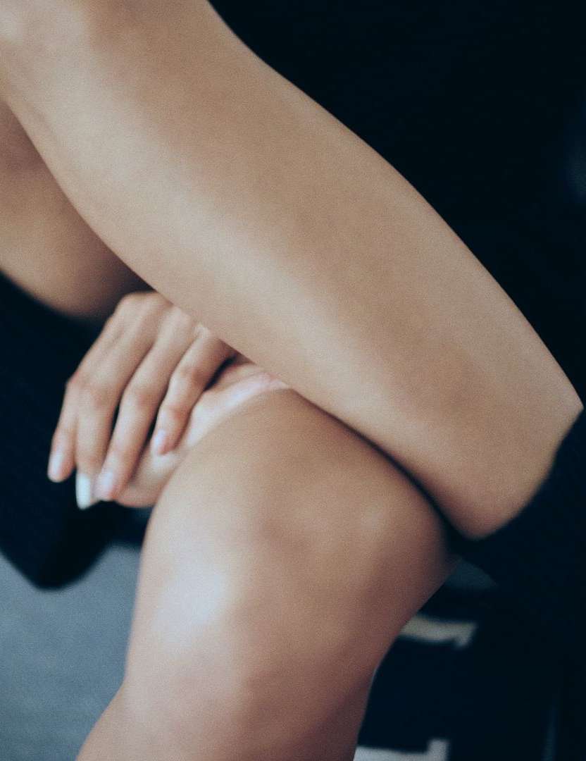 Close-up studio shot of an adult female with crossed arms and legs, showing the texture and form of her skin against a dark backdrop.