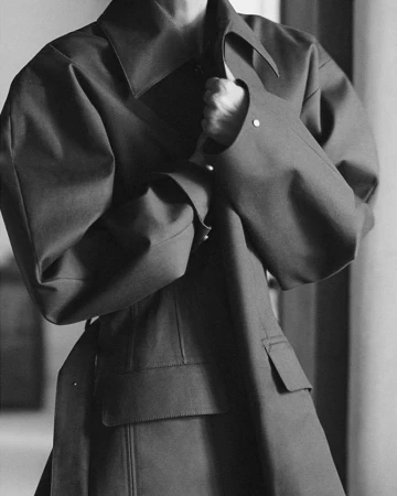 Monochrome portrait of a person wearing a structured collared coat with belted waist photographed by Chris Colls