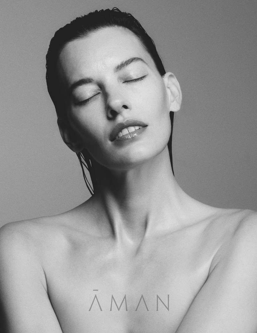 Monochrome close-up of a beautiful Caucasian woman with eyes closed, wet hair, bare shoulders against a simple grey background.