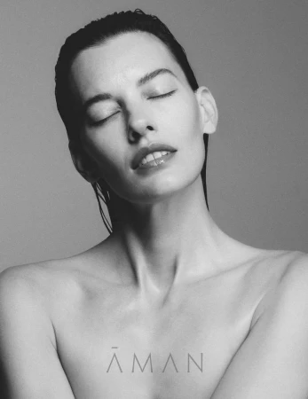 Monochrome close-up of a beautiful Caucasian woman with eyes closed, wet hair, bare shoulders against a simple grey background.