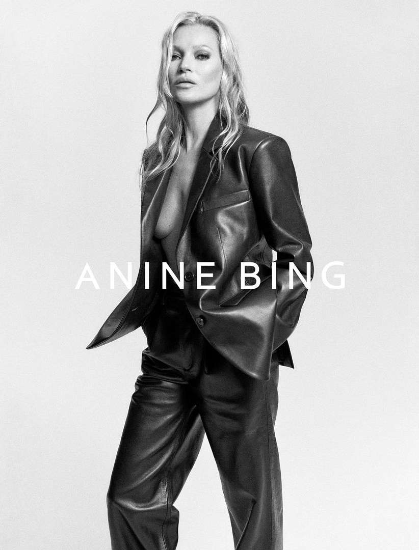 Black and white fashion portrait of Kate Moss in a black leather suit against a bright backdrop, featuring the 'Anine Bing' logo.