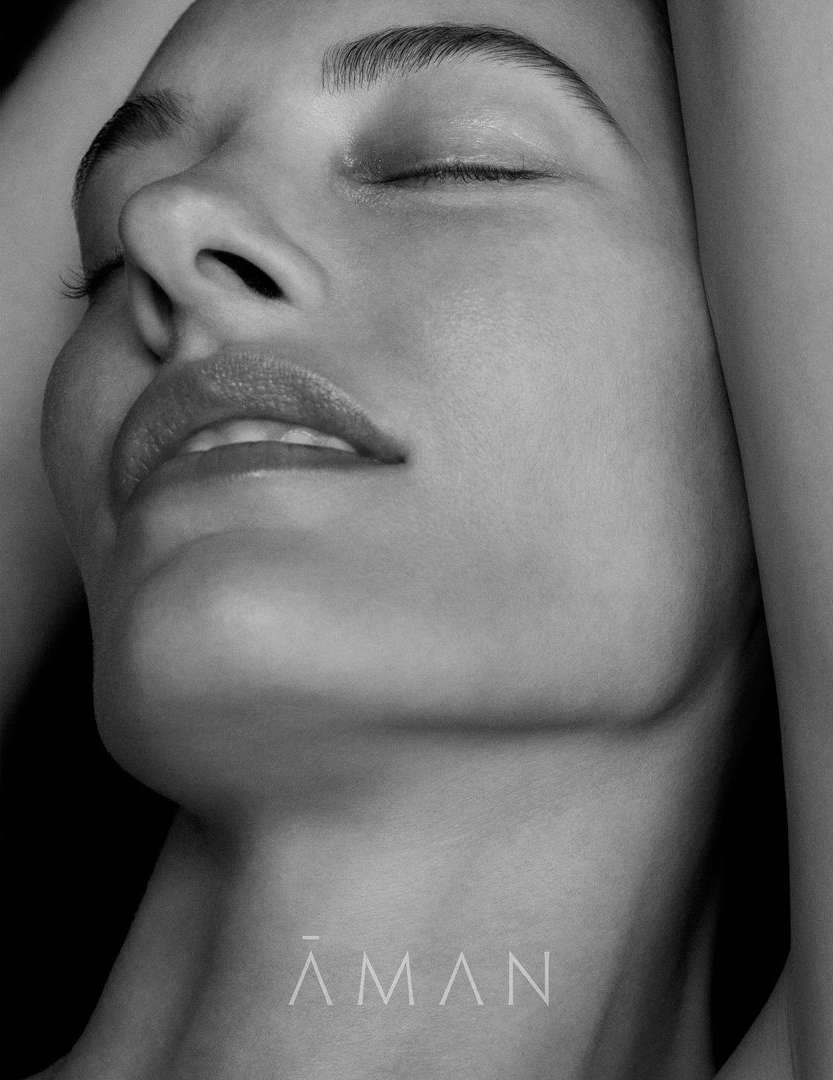 Monochrome close-up portrait of a woman with eyes closed and arms raised against a dark background by photographer Chris Colls.