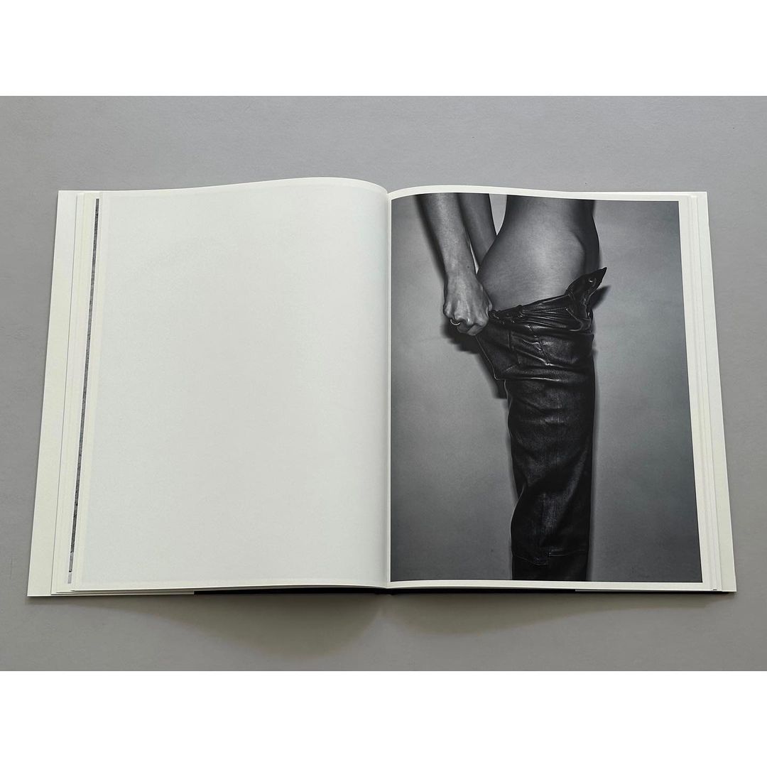 Open book shows a grayscale image of an adult wearing leather pants, viewed at eye-level, in a photo studio setting.