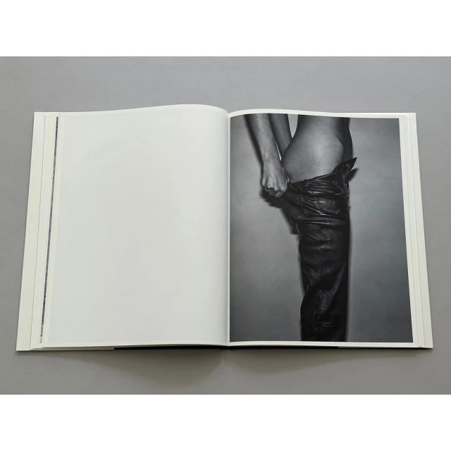 Open book shows a grayscale image of an adult wearing leather pants, viewed at eye-level, in a photo studio setting.