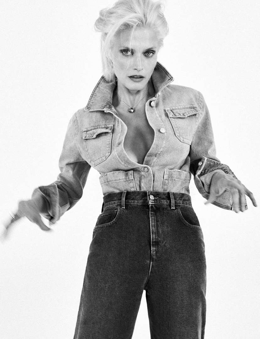 Monochrome portrait of a blond woman wearing a denim jacket and dark high-waisted jeans against a plain background