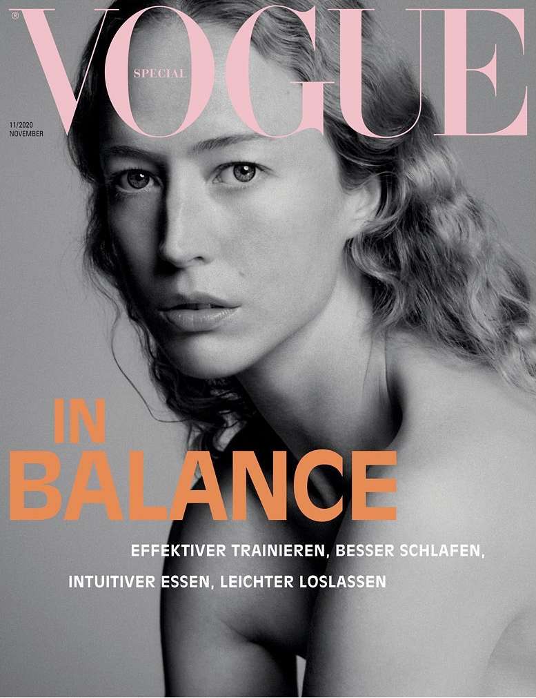 Close-up portrait of a woman with long wavy hair against a grey background, featuring large pink VOGUE masthead typography.