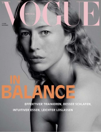 Close-up portrait of a woman with long wavy hair against a grey background, featuring large pink VOGUE masthead typography.