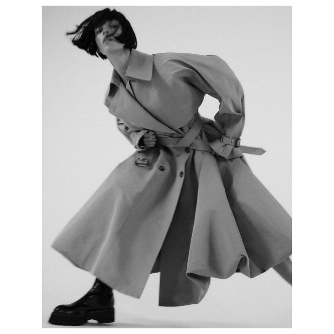 Model in a flared trench coat and dark boots posing dynamically against a white background