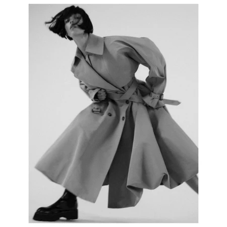 Model in a flared trench coat and dark boots posing dynamically against a white background