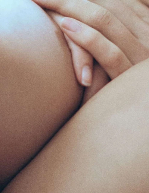 Close-up on a hand gently resting on the crossed legs of an adult female in a softly lit, neutral setting.