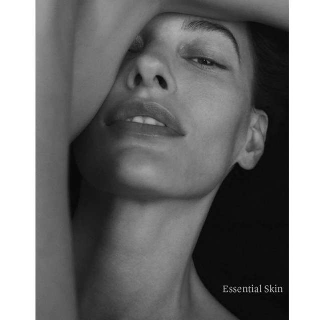 Close-up black and white portrait of an adult female with hand on head. Shadowed black background. Beauty, skincare, fashion.
