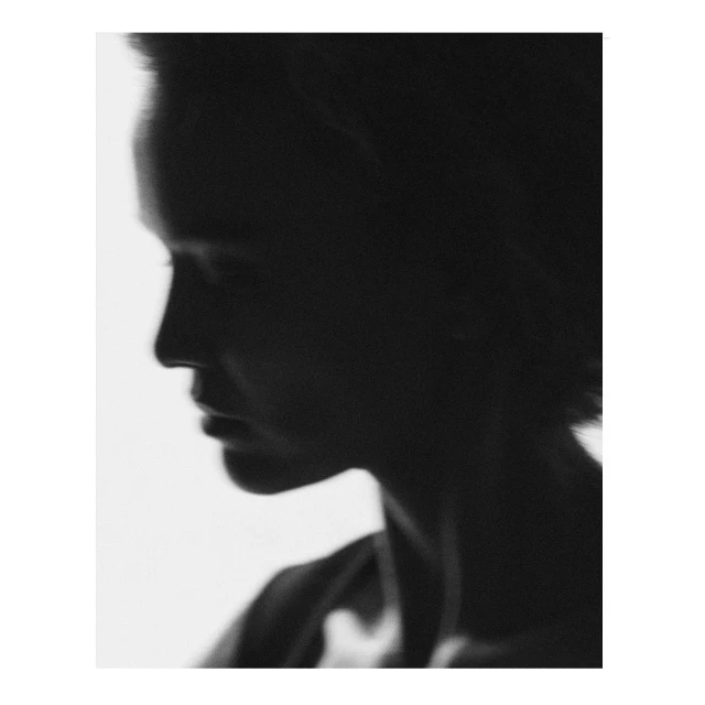 Monochrome portrait of an adult woman in profile, with dark hair, against a bright background in a studio setting with soft light.