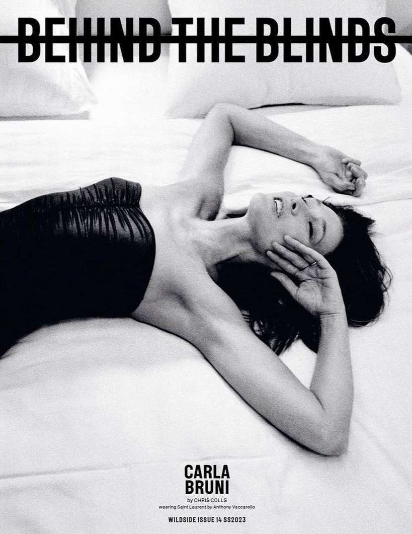 Black and white portrait of a woman lying on her back on a bed with a black top, eyes closed, and arm raised to her face.