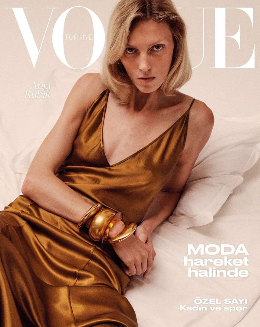 Vogue Türkiye cover featuring Anja Rubik in a gold dress, lying on a bed. The image is a medium shot with a soft, diffused lighting.