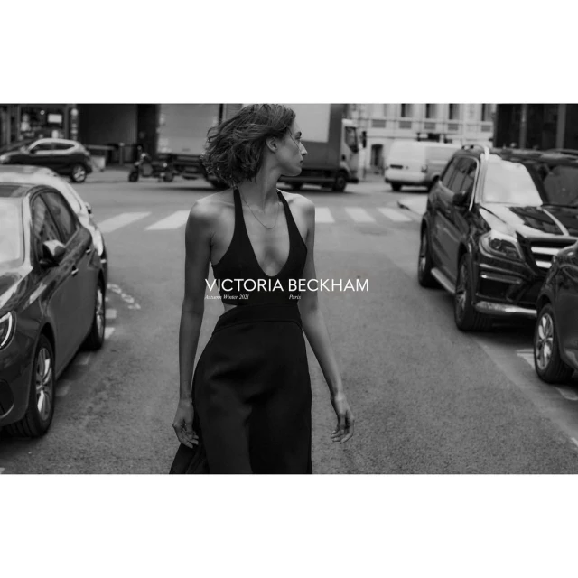A woman in a black dress walks on a crosswalk between cars in a black and white outdoor urban fashion photography setting.