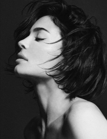 Black and white portrait of a woman with short dark hair in profile against a dark background, photographed by Chris Colls.
