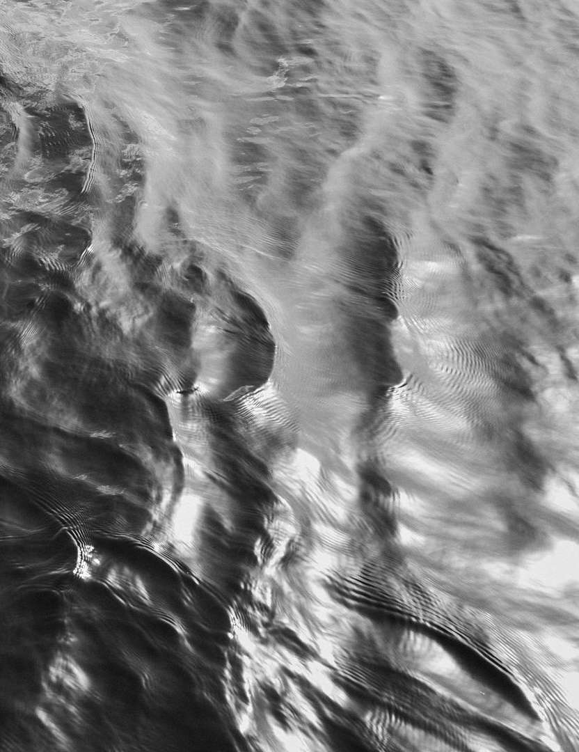 Abstract black and white photography of water ripples creating dynamic patterns, with a shallow depth of field and monochromatic palette.