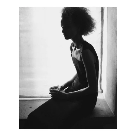 Black and white portrait of a woman seated near a window holding a glass, photographed by Chris Colls.