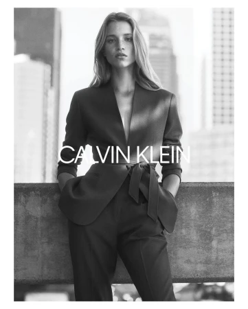 Black and white portrait of a female model wearing a tailored belted blazer and trousers against an urban rooftop background.