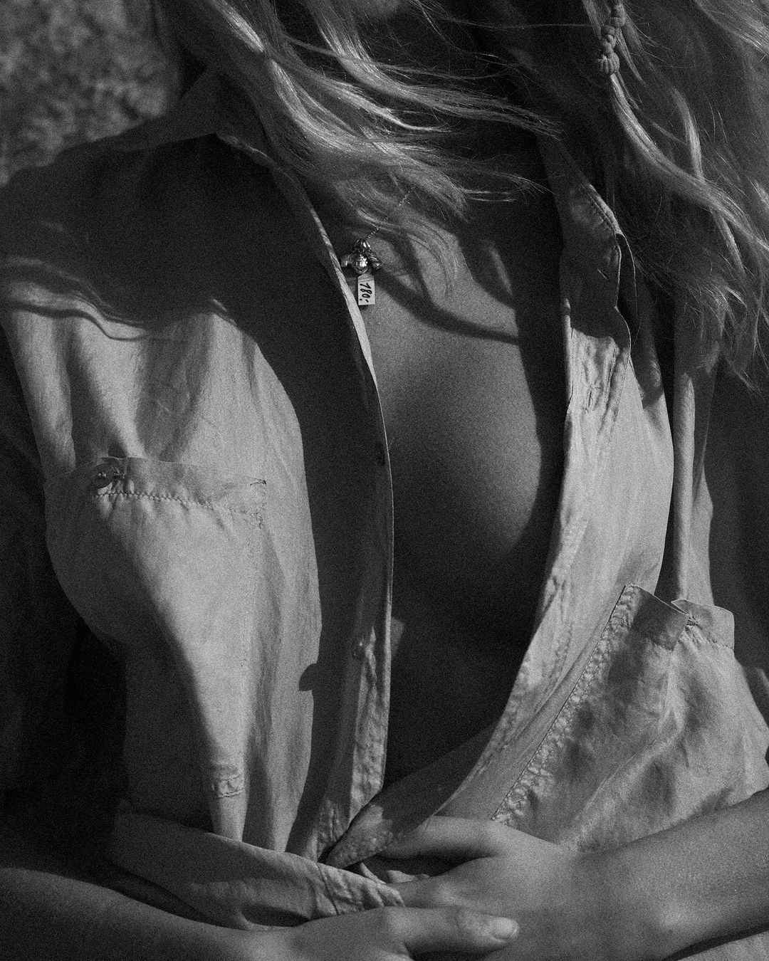 Monochrome portrait of a woman wearing an unbuttoned shirt and a small pendant necklace, photographed by Lachlan Bailey.