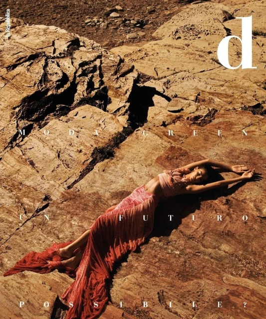 Woman in flowing dress on rocks for magazine cover, editorial fashion photography, desert landscape backdrop, bright natural lighting.