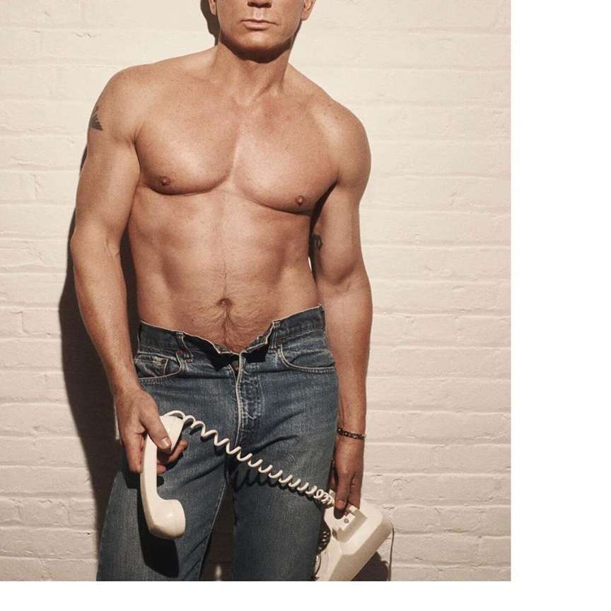 Shirtless adult male in jeans holding a vintage telephone in a studio environment with a white brick wall background. Fitness and health.