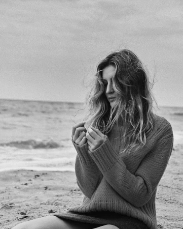Black and white portrait of a woman with long wavy hair wearing a ribbed knit sweater on a sandy beach