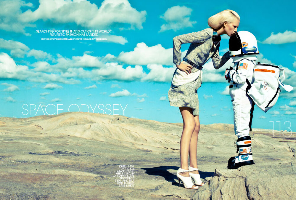 Fashion shot features a slender woman in a dress and heels kissing an astronaut in full gear against a sky and sandy landscape.