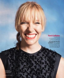 Portrait of Toni Collette with blonde bangs wearing a black embellished top against a sky blue backdrop