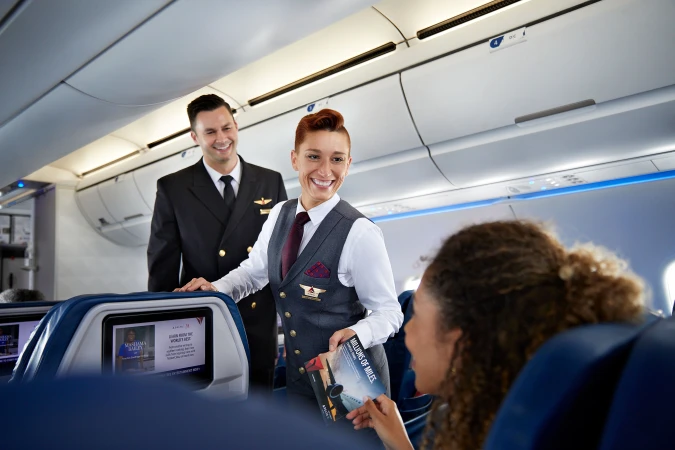 Cabin crew member assisting passenger inside a Delta airplane. Smiling flight attendant offers in-flight information to traveler.