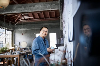 Man wearing round glasses and a blue denim shirt holding a ceramic piece inside a workshop by eszter + david