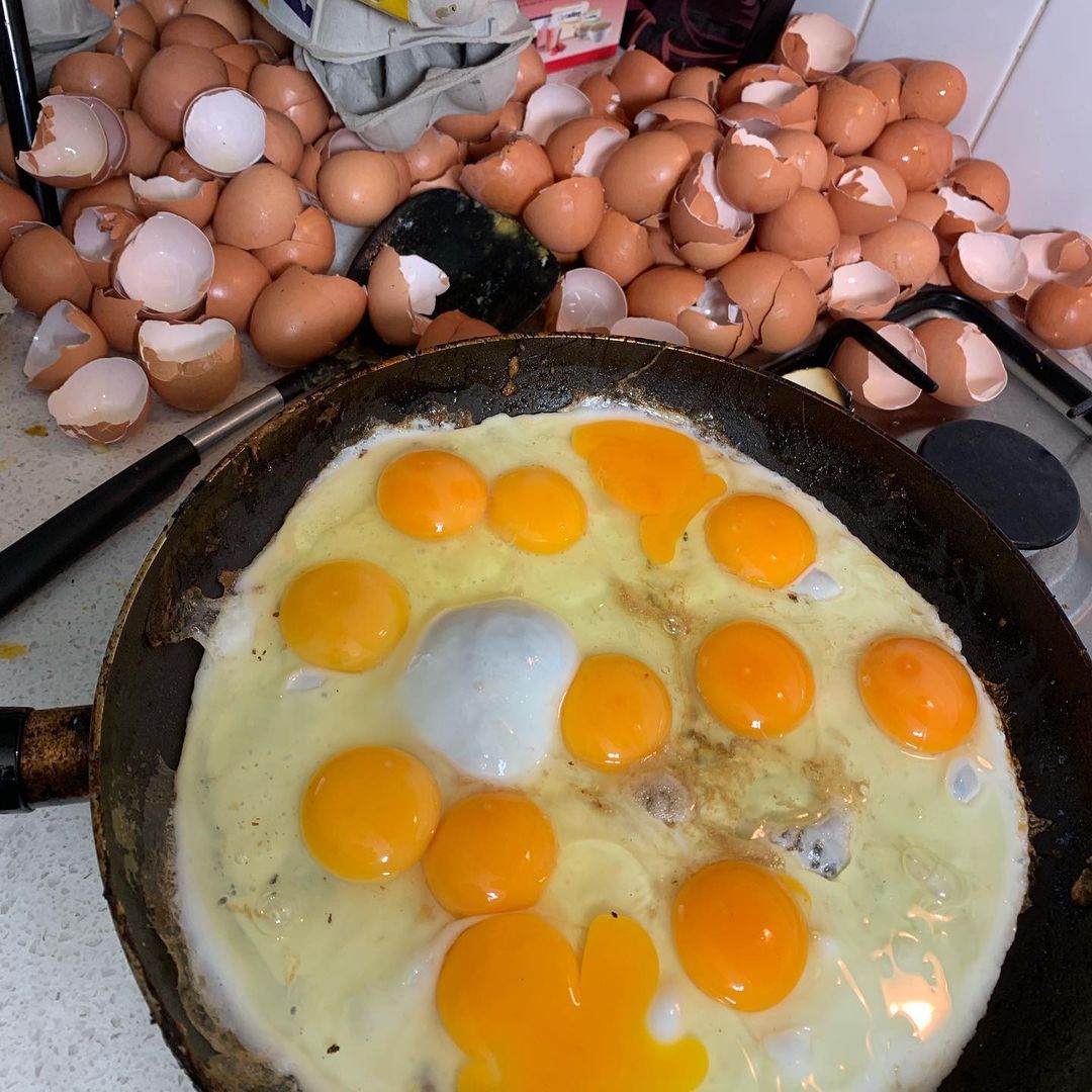 Close-up of fried eggs in a pan surrounded by a pile of eggshells, showcasing food preparation and potential cooking mishaps.