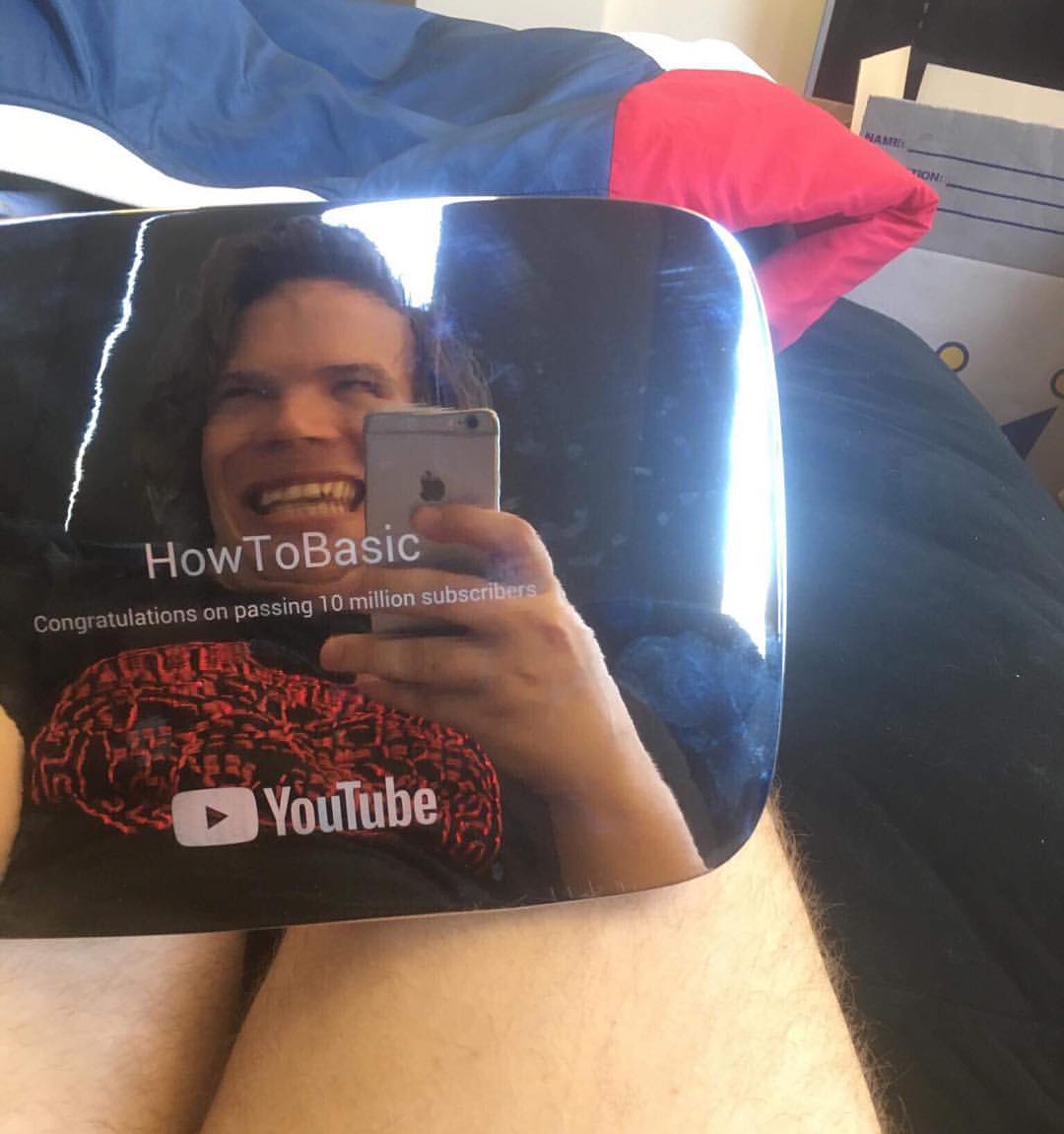 A man takes a selfie while holding a YouTube Creator Award plaque for passing 10 million subscribers; the plaque reflects his image.