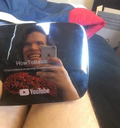 Man holding a reflective plaque with YouTube logo, taking a mirror selfie in a domestic bedroom setting.