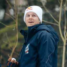 Man wearing a white beanie and a dark blue winter jacket holding a snowball outdoors