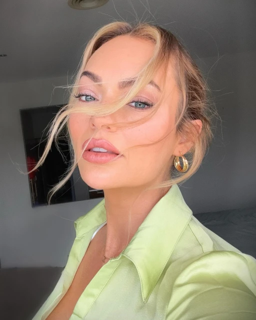 Close-up portrait of a blonde woman wearing a green collared shirt and gold hoop earrings, with soft lighting and blurred background.
