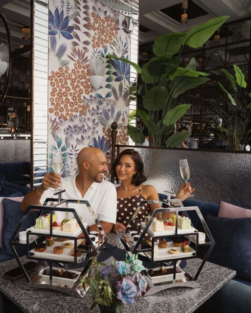 A happy couple enjoys an afternoon tea with champagne in a restaurant. Tiered stands with pastries and desserts are on the table.