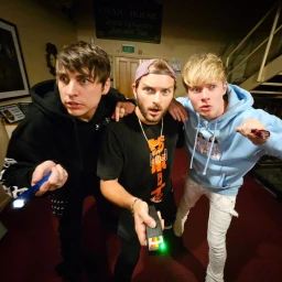 Three men holding flashlights and equipment indoors with a surprised expression