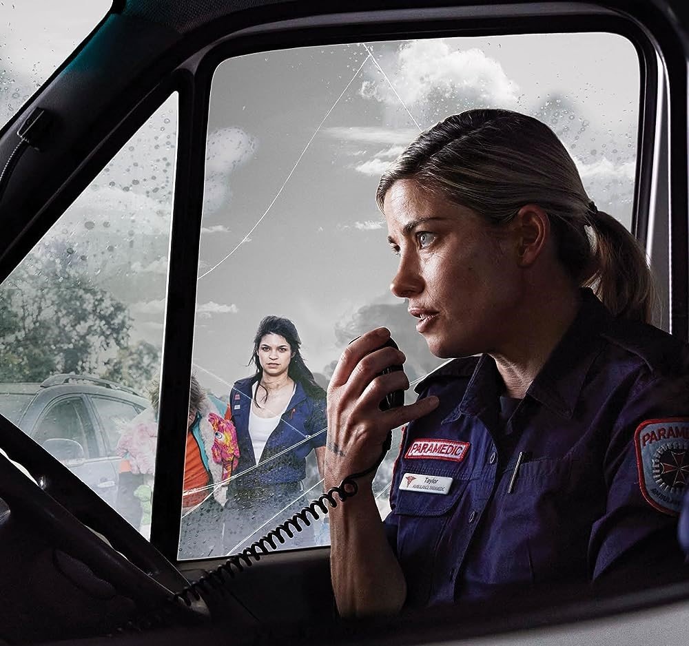 Paramedic in uniform using radio inside vehicle, woman in background, potential rescue or emergency response scene, outdoor environment.