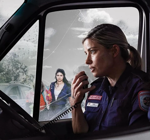 Paramedic in uniform using radio inside vehicle, woman in background, potential rescue or emergency response scene, outdoor environment.