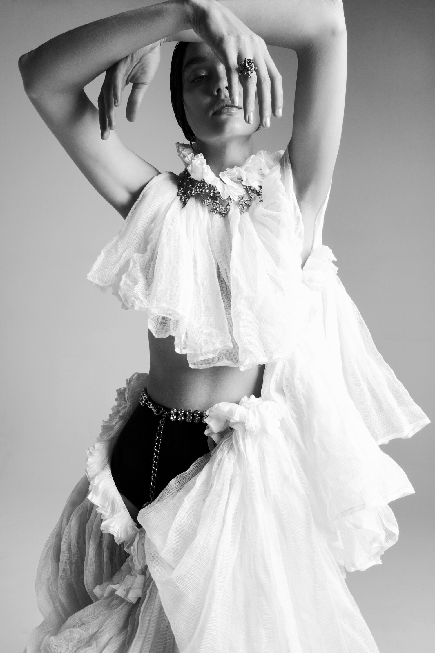 Fashion photo of a woman in a white ruffled garment, black bottoms, and jewelry. The model poses against a neutral background.