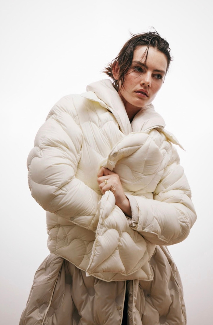 Woman in off-white puffer coat, neutral background. Fashion shot with soft, diffused lighting and cool color palette.