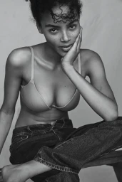 Monochrome portrait of a young Black woman with curly hair wearing a bra and jeans, resting her hand on her cheek.