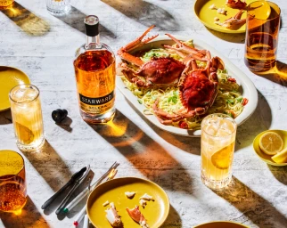 Overhead food styling shot featuring a bottle of Starward whisky next to a platter of pasta with whole crabs and tall cocktail glasses