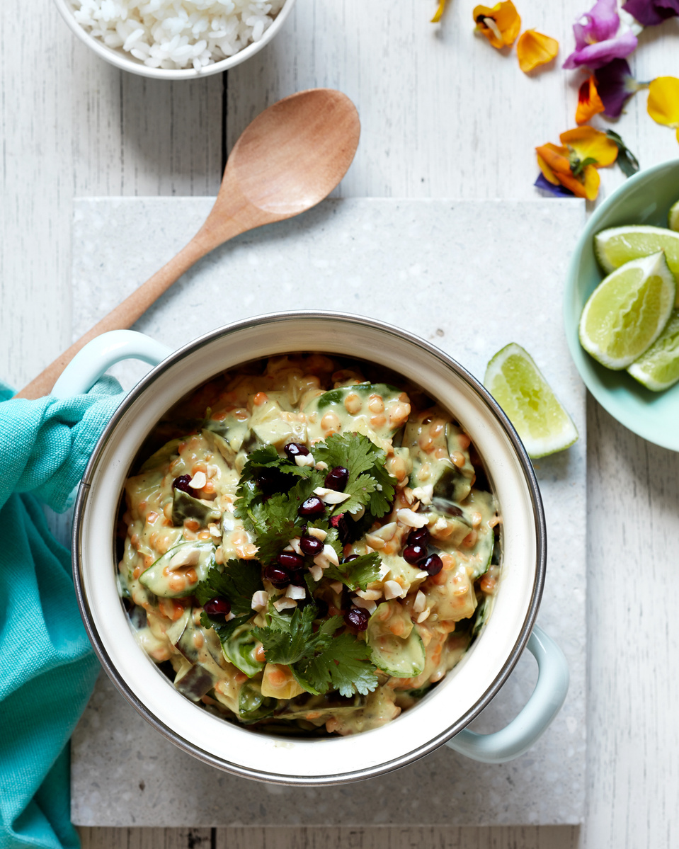 Overhead shot of a pot filled with Indian curry with rice and lime wedges, presented on a rustic white wooden table.