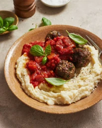 Close-up overhead shot of meatballs in tomato sauce over creamy mashed potatoes in a ceramic bowl, styled by Jamie Humby
