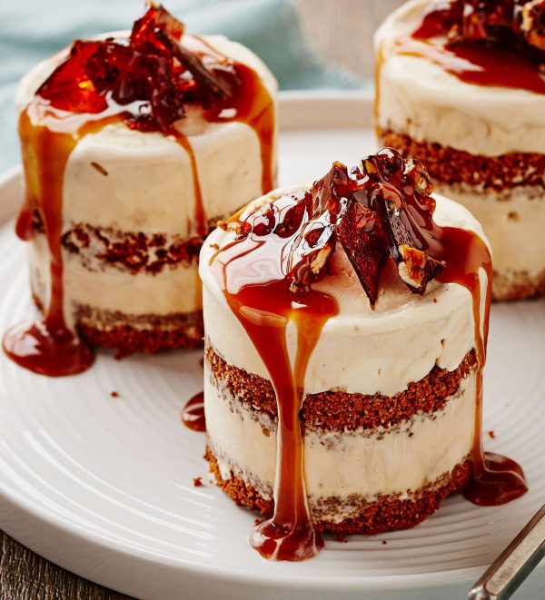 Three individual cakes are displayed with cream frosting, garnished with amber-colored brittle and caramel sauce on a white plate.