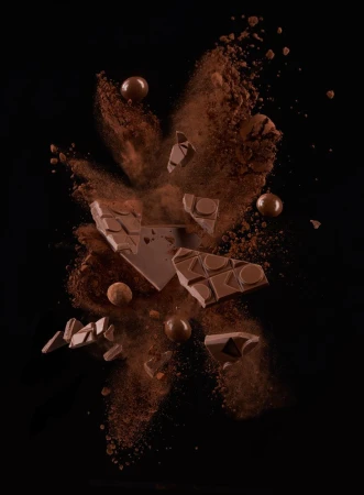 Flying milk chocolate chunks and spheres explode with cocoa powder against a black backdrop, creating a visually appealing food still life.