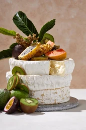 Stacked rounds of white bloomy rind cheese topped with exotic fruits and kiwi slices styled in Melbourne.