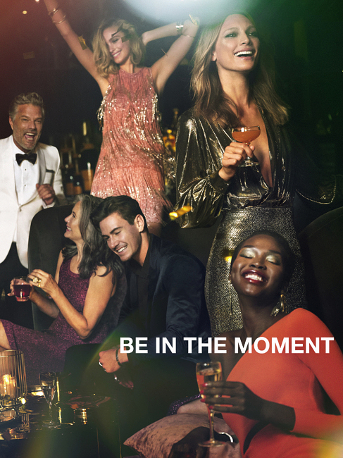 Several people celebrate together at a party. The group is dressed in formal attire, with some holding drinks and smiling.
